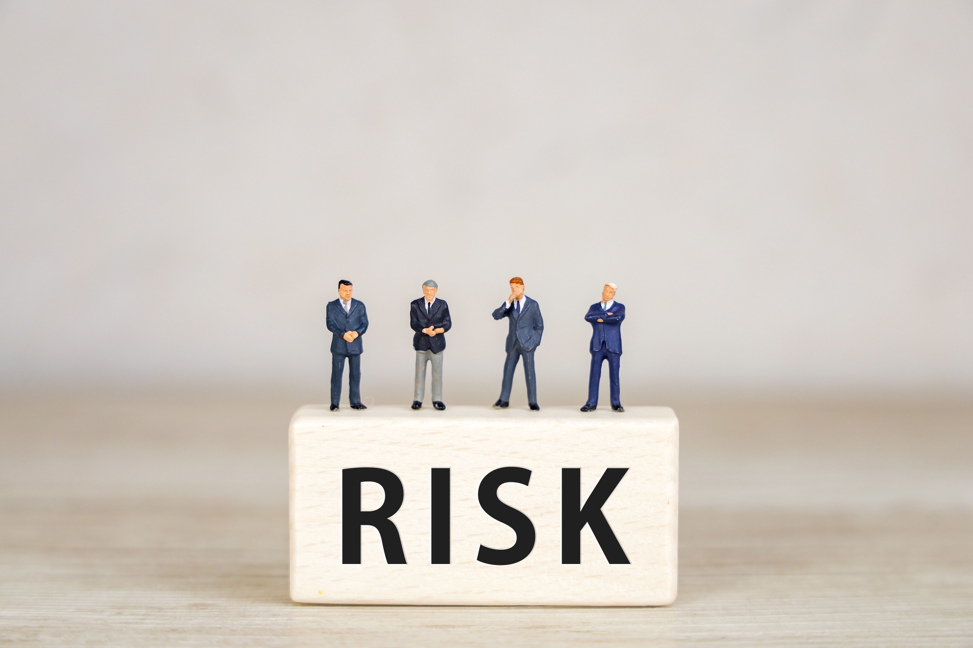 「RISK」と書かれたブロックの上に立つミニチュアのビジネスマンたち