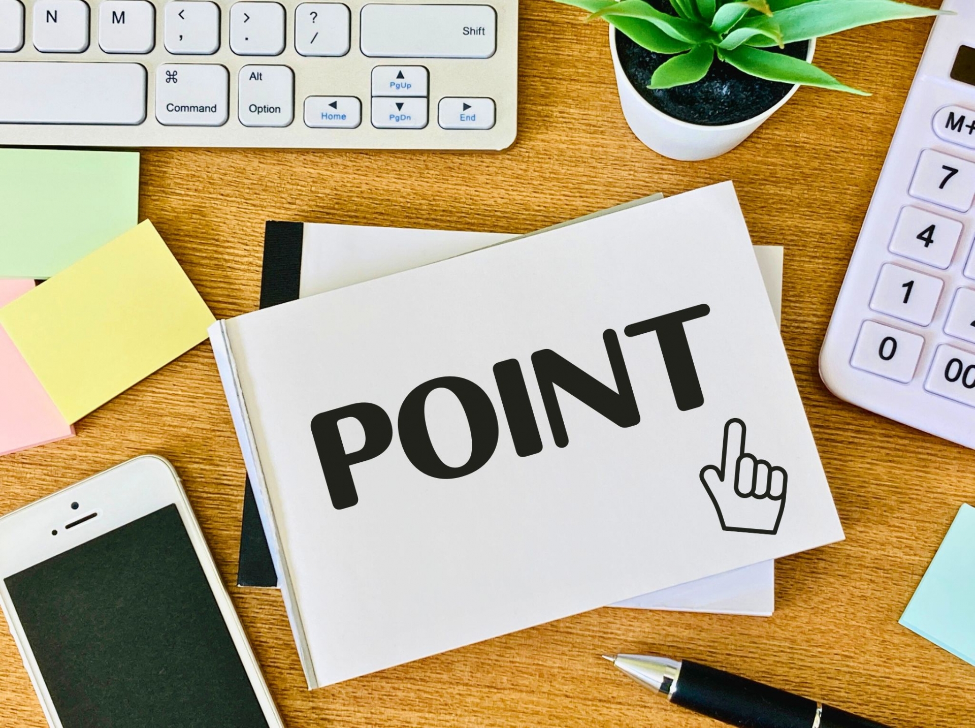「POINT」と書かれたノートが置かれた、キーボードや電卓のあるデスクの画像