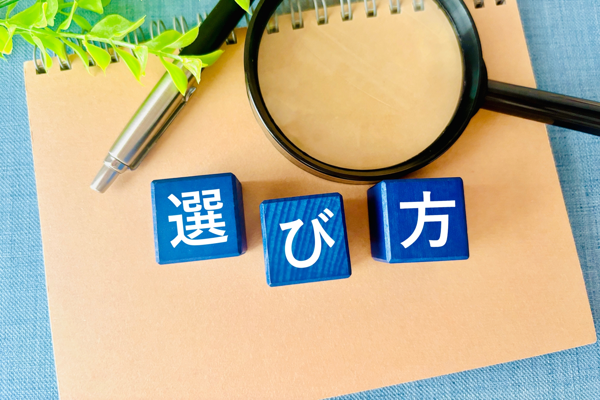 「選び方」と書かれた木製のブロックが、ノートと拡大鏡の前に置かれている。何かを選択する際の具体的な方法や手順を説明するイメージ。