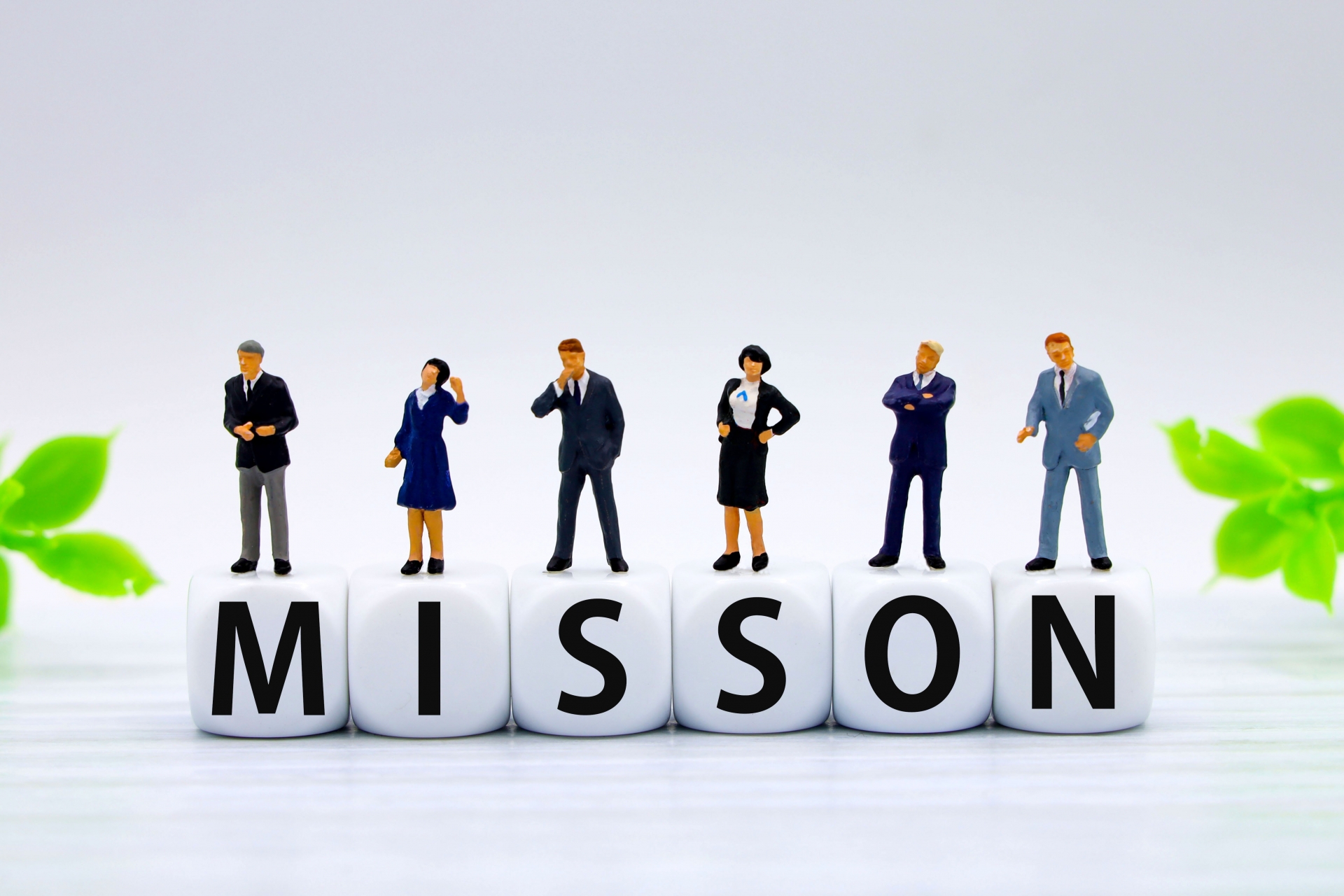 ビジネスパーソンのミニチュア人形が立つ「MISSION（使命）」の文字ブロック