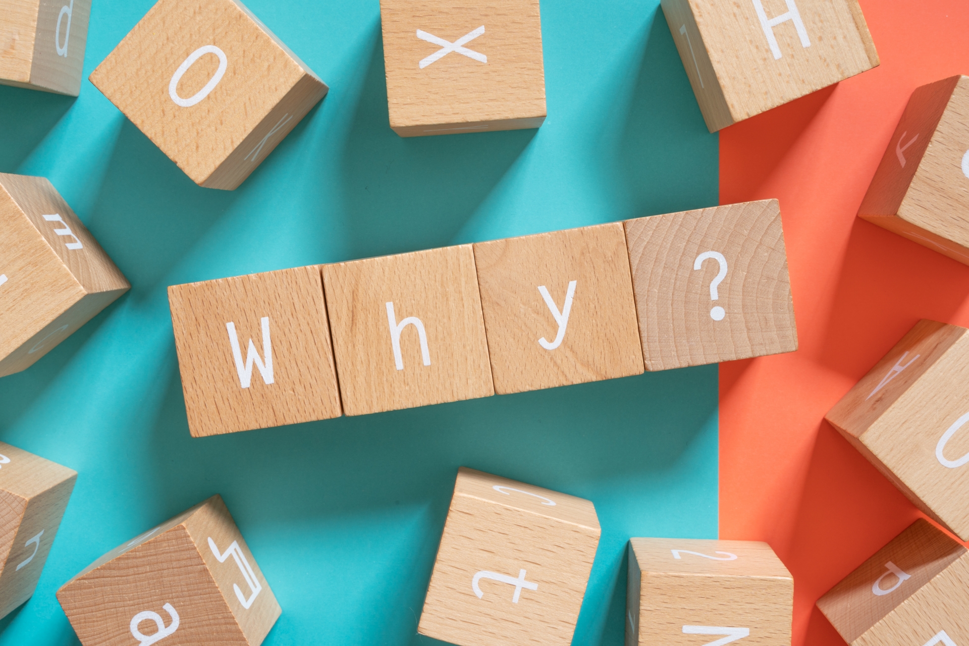 なぜを意味する「Why」と書かれた木製ブロックと疑問を表現する「？」マーク