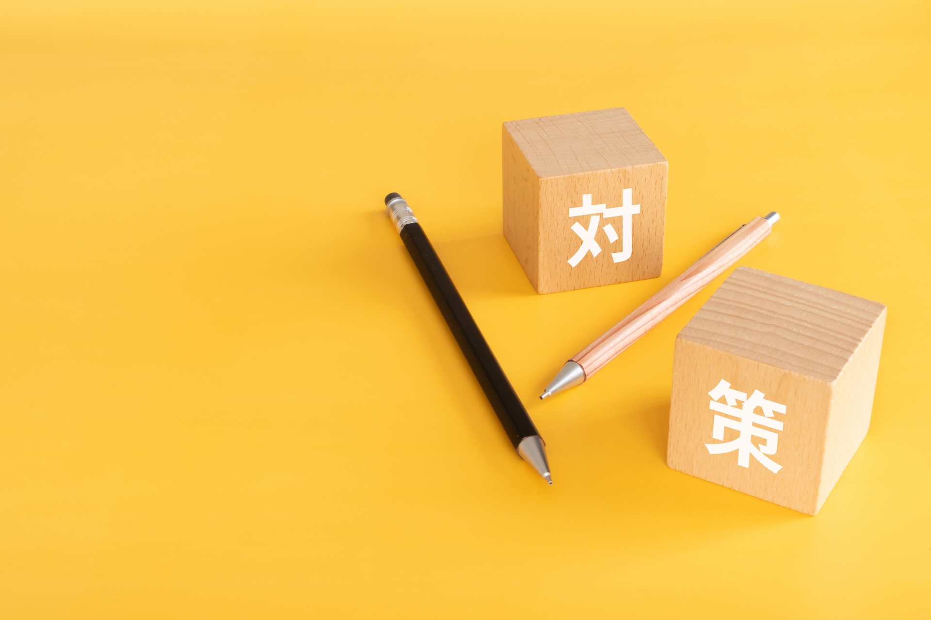 黄色い背景の上に置かれた「対策」と書かれた木製ブロックと鉛筆