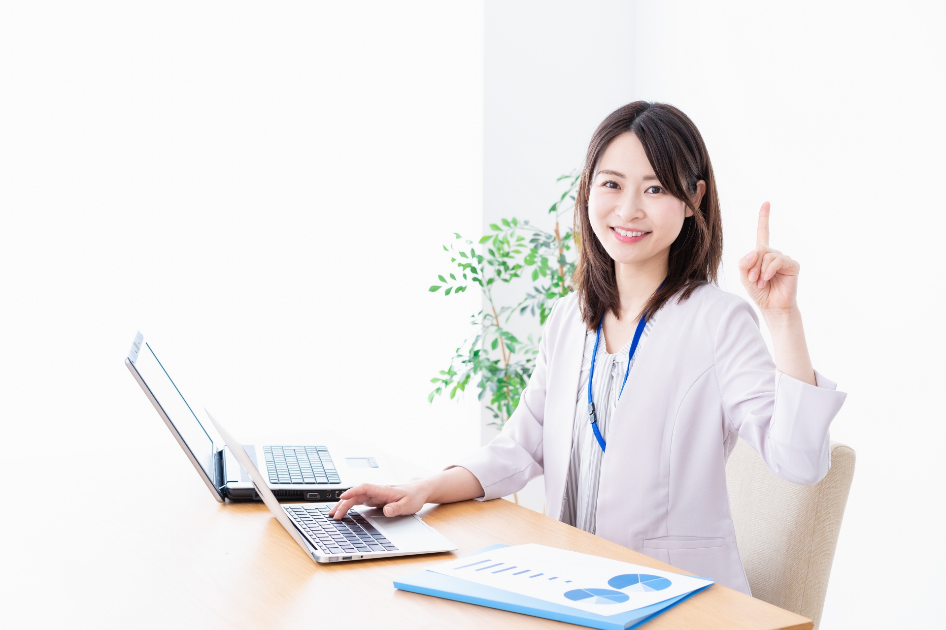 オフィスでノートパソコンを操作しながら、指を立ててアイデアや提案を説明している笑顔の女性。