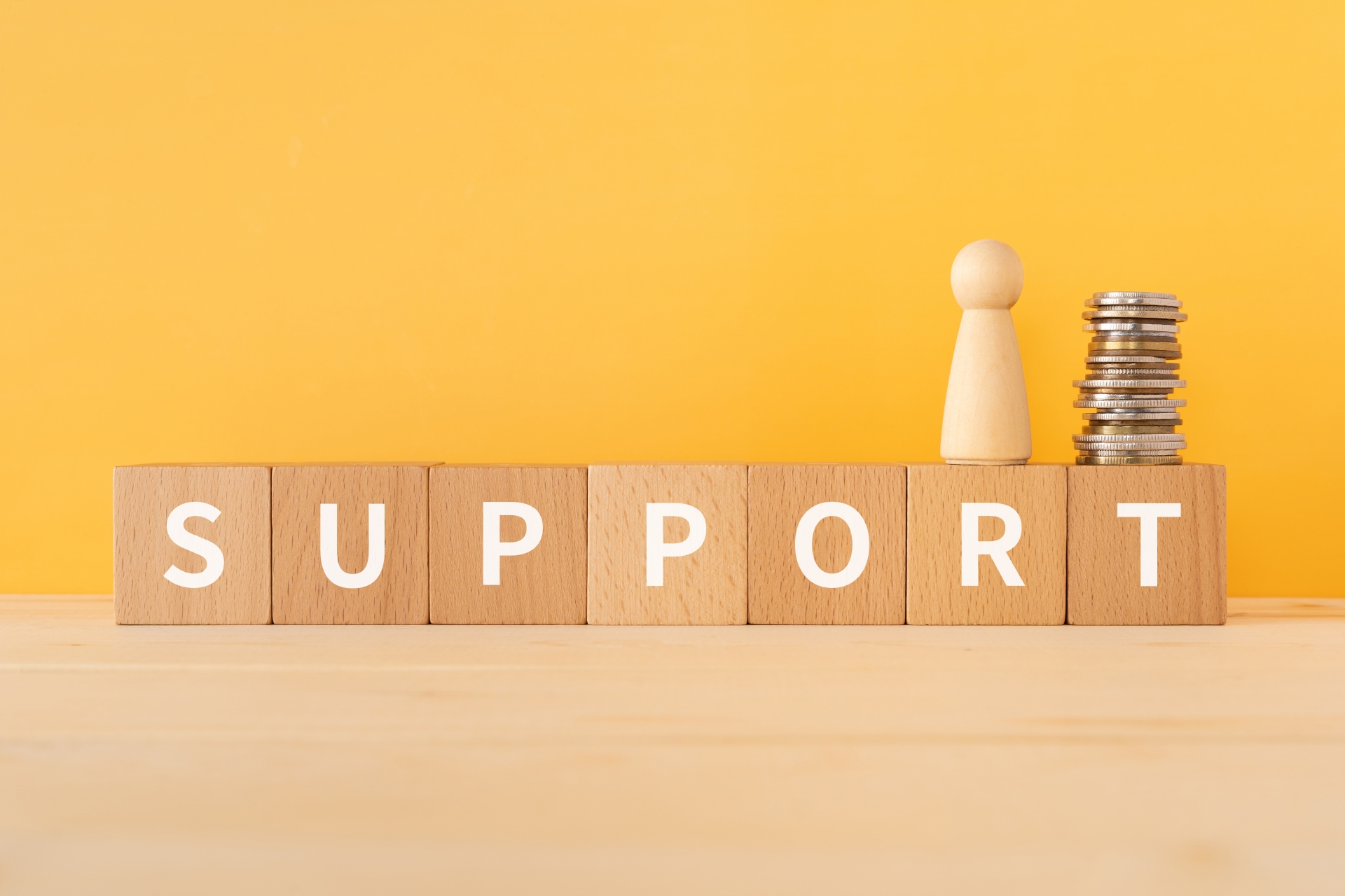 「SUPPORT」の文字ブロックと積み重ねられたコイン