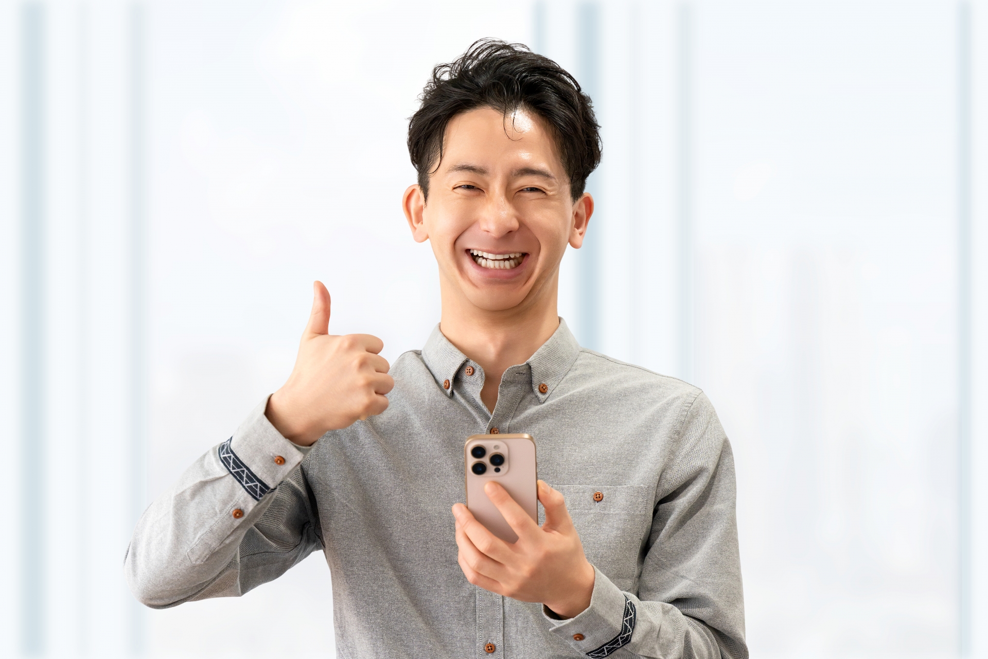 スマートフォンを持ち、笑顔で親指を立てるスーツ姿の男性