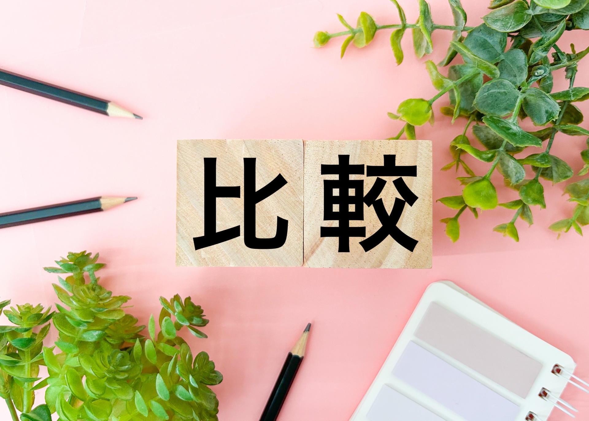 「比較」と書かれた木製ブロックと植物、文房具のデスクイメージ