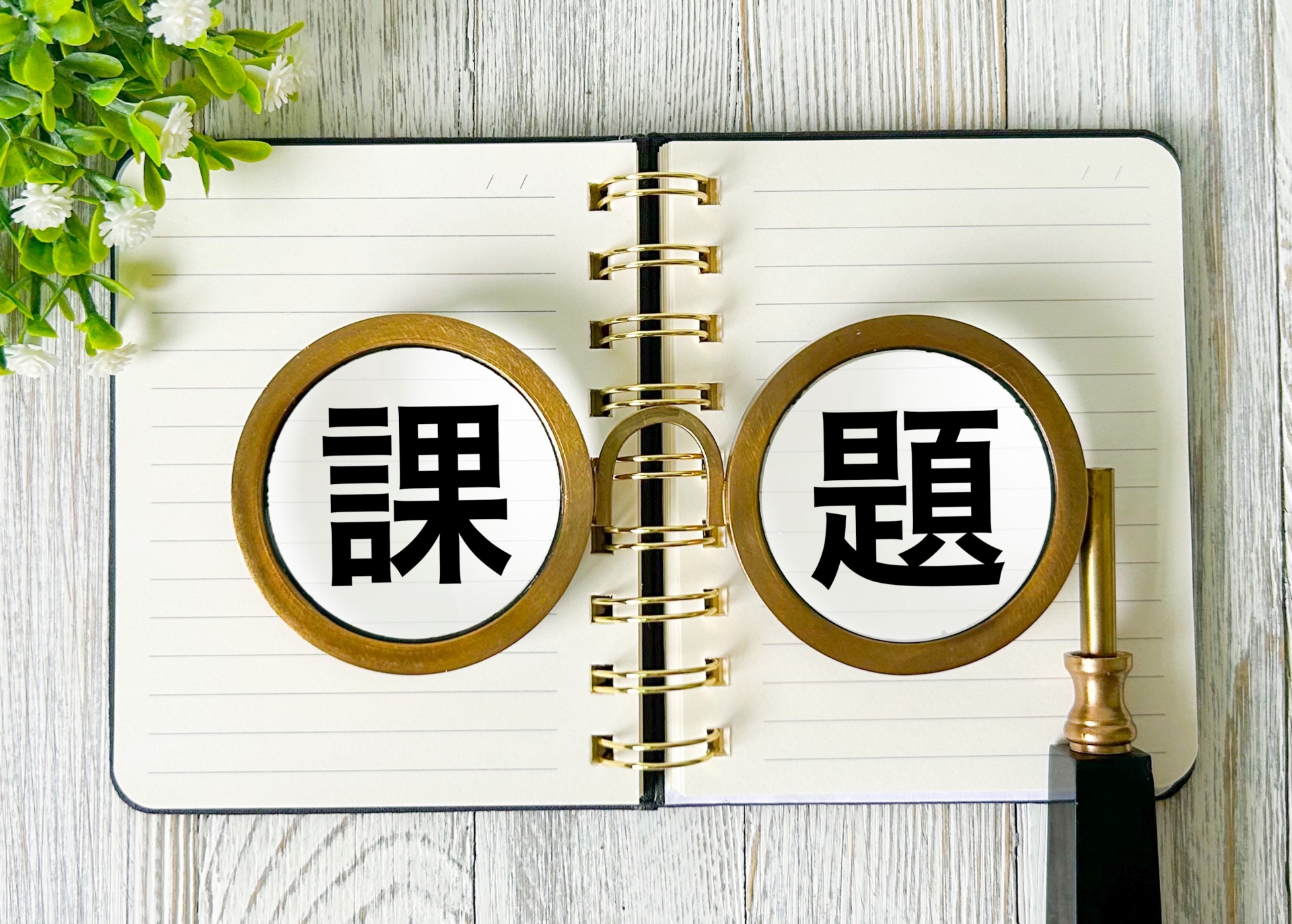 課題を意味する「課題」の文字と虫眼鏡が描かれたノート