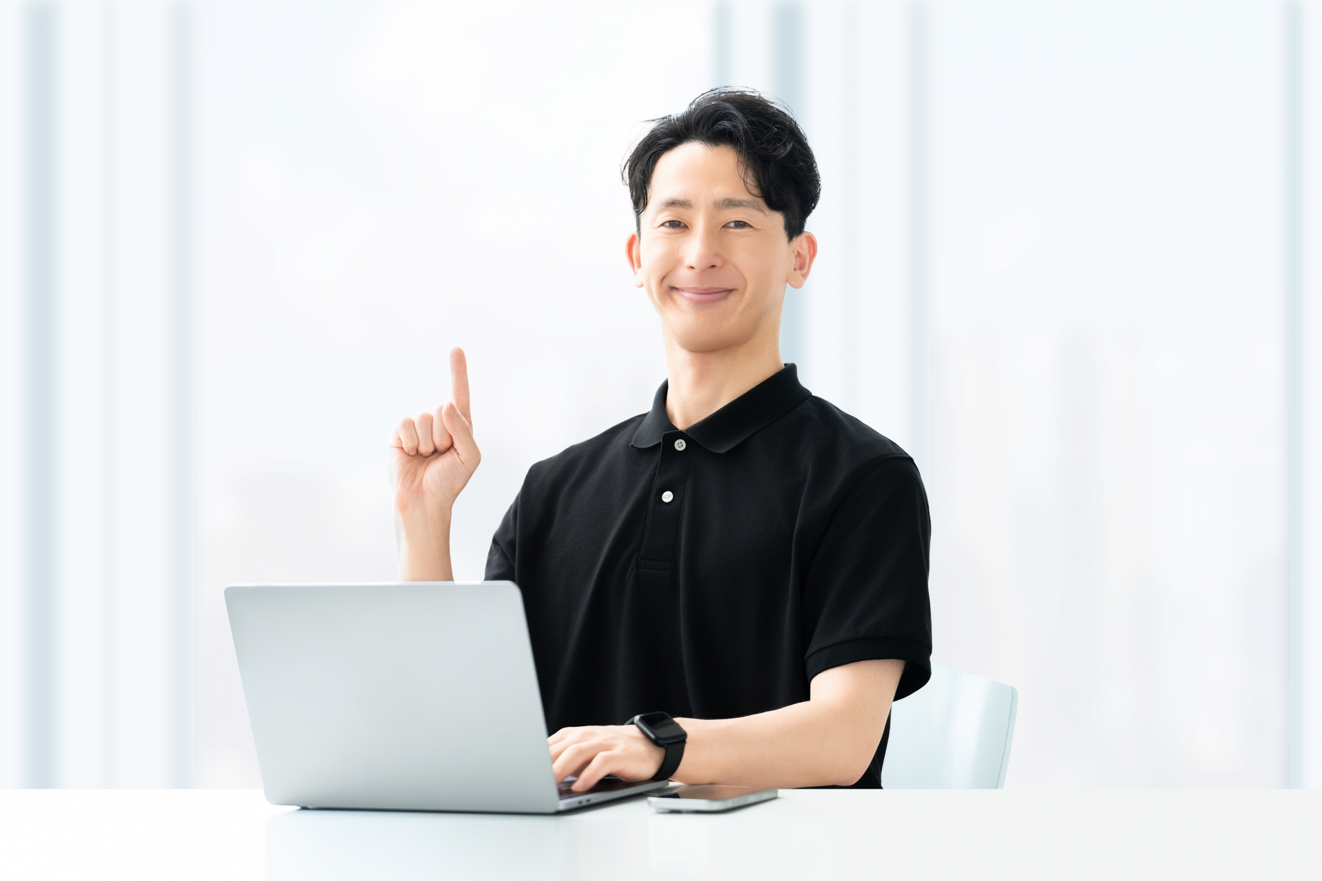 PCを操作しながら、何かを思いついたように指を立てる笑顔の男性