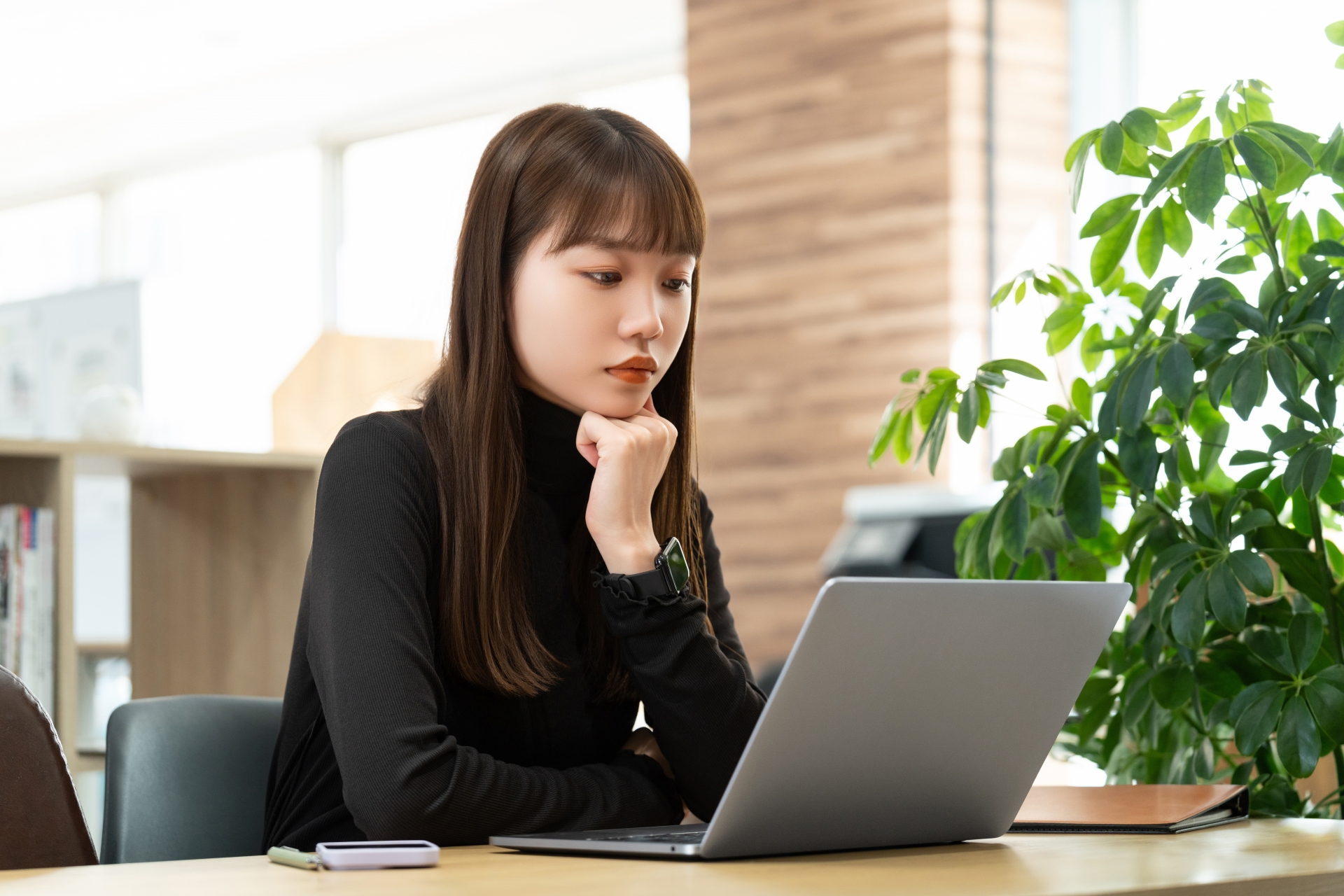 オフィスでノートPCを見ながら考え事をする女性