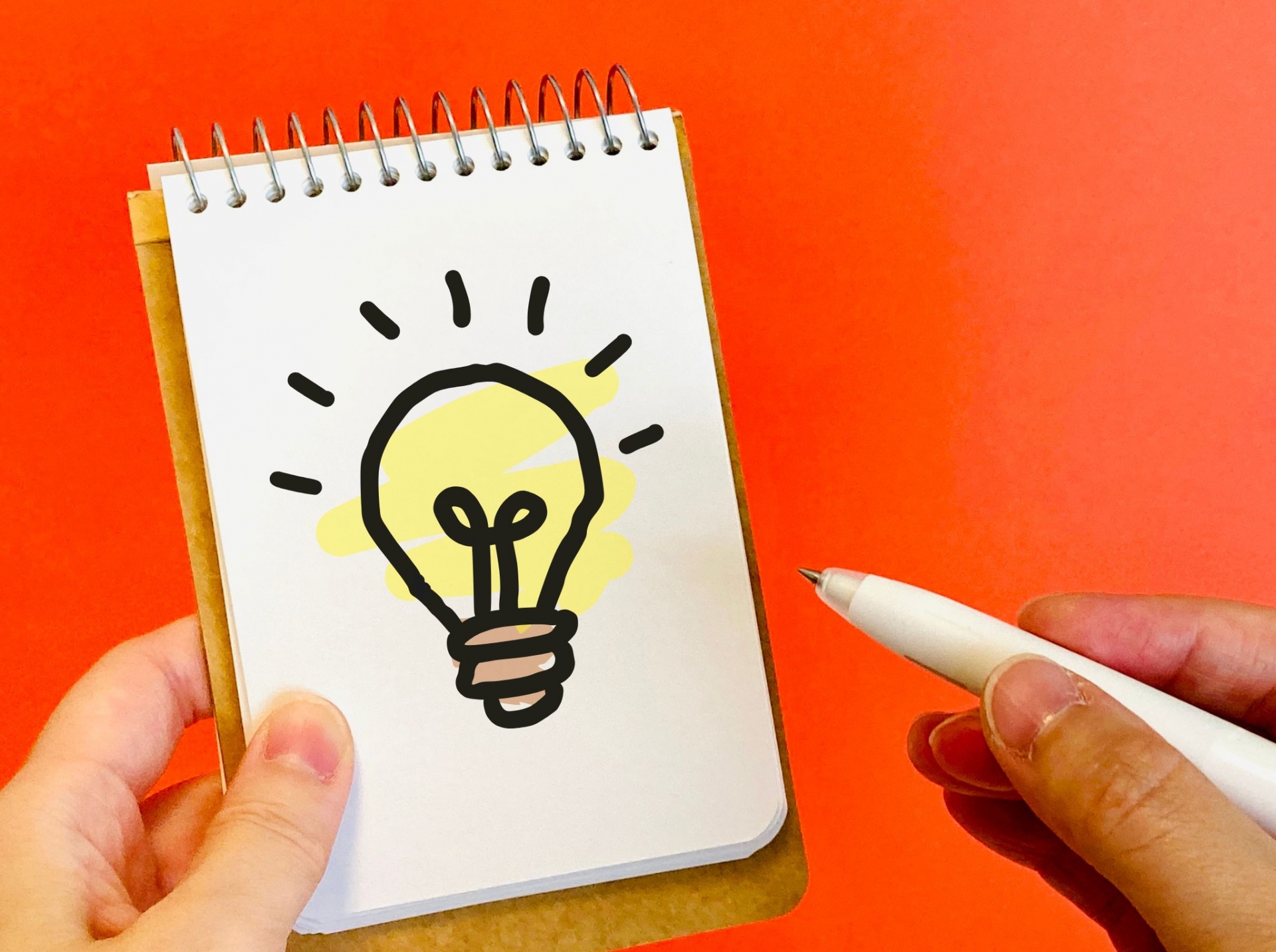 アイデアを意味する、電球が描かれたノートとペンのイメージ