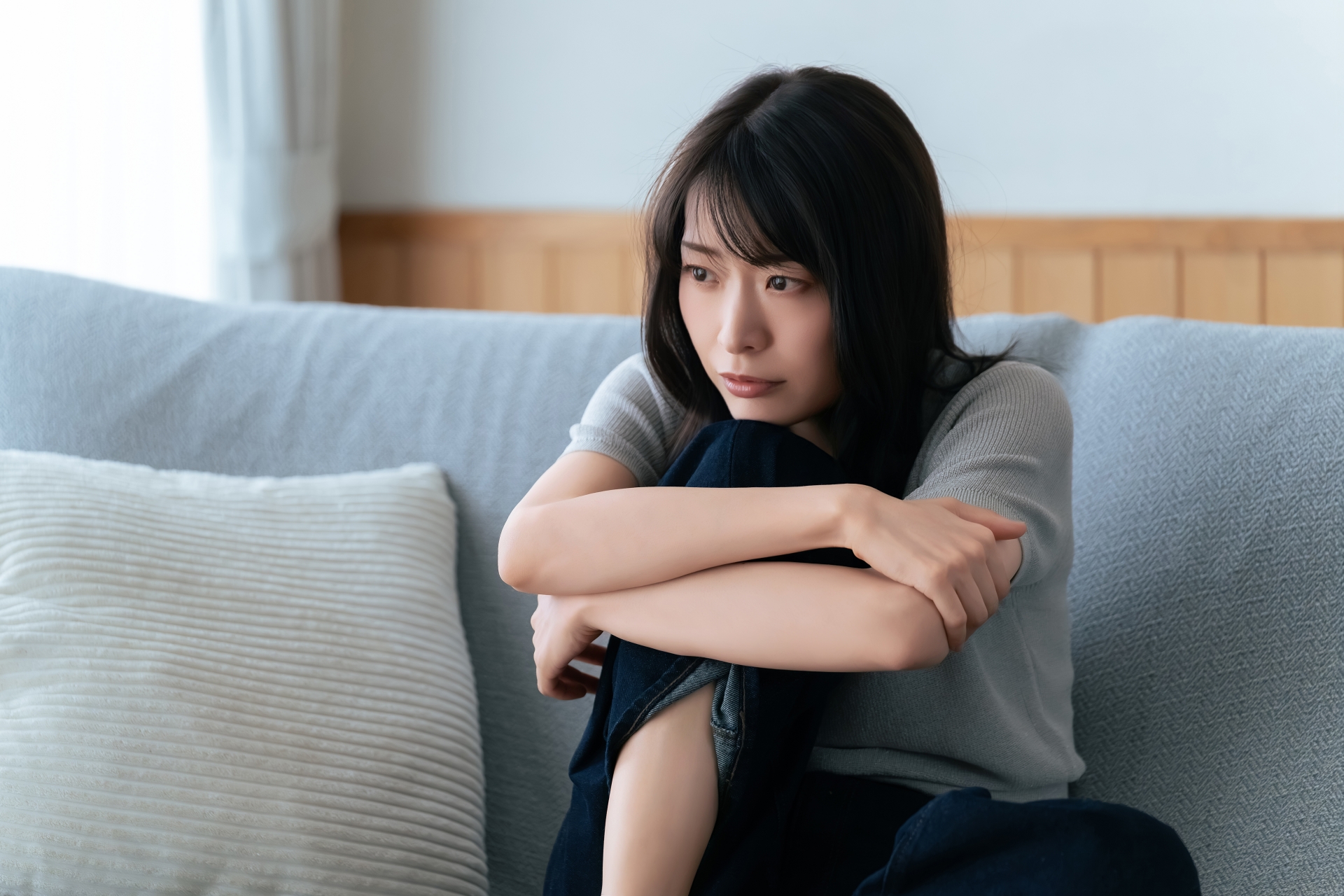 ソファで膝を抱えて座り、少しうつむいている女性