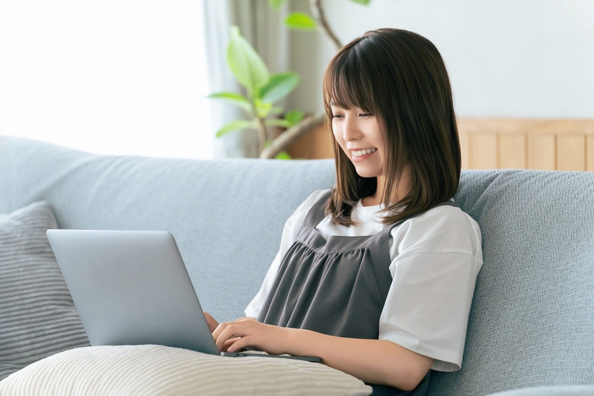 自宅のソファでくつろぎながらノートPCを使う女性