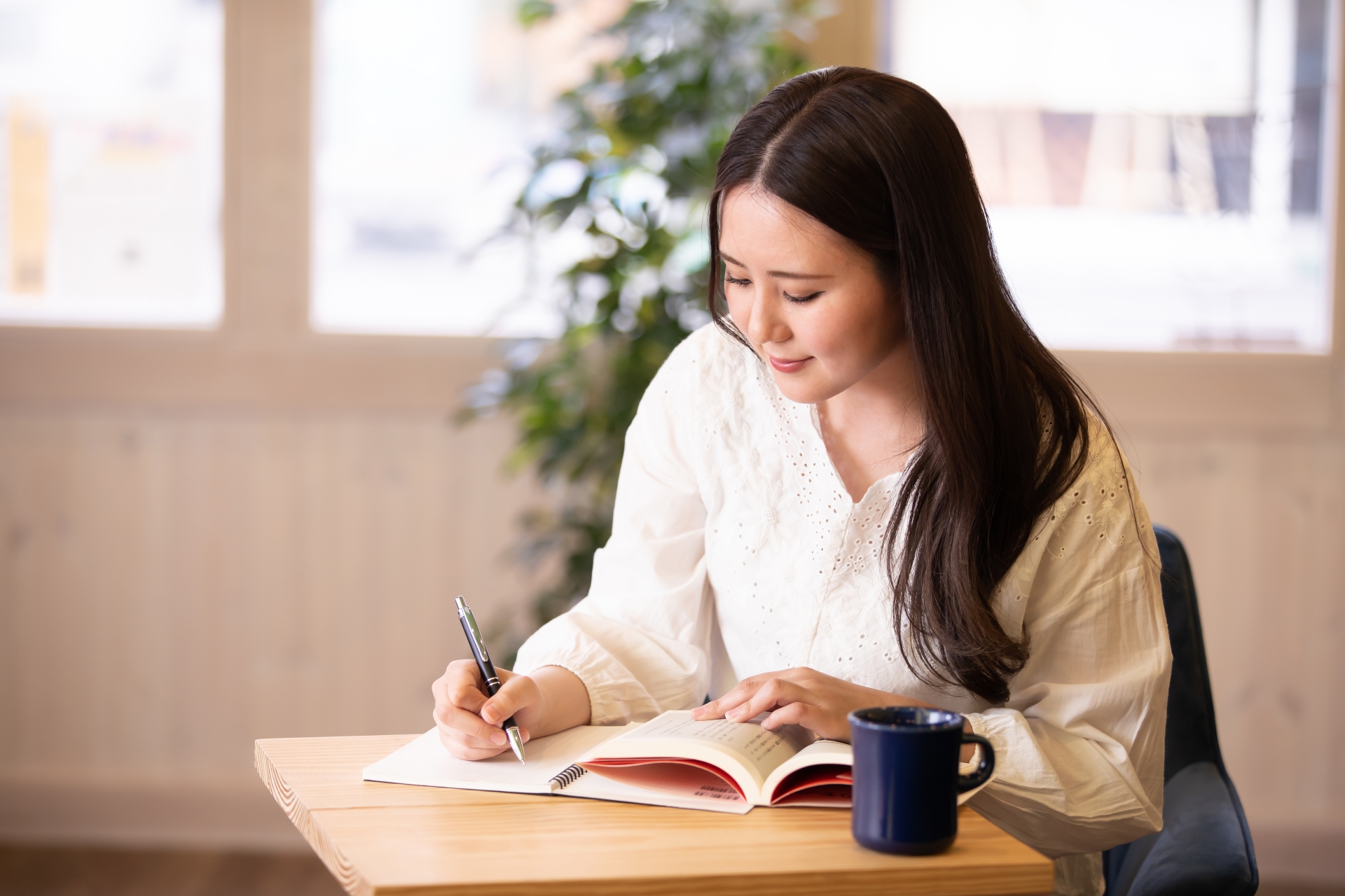 カフェでノートに書き込みながら本を読んでいる女性